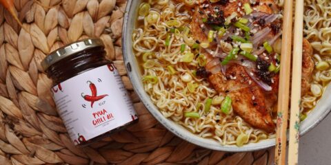 a bowl of noodles with meat and vegetables next to chopsticks