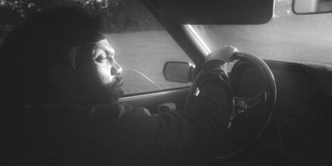 a man sitting in a car with his hand on the steering wheel