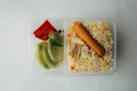 a plastic container filled with rice and a hot dog