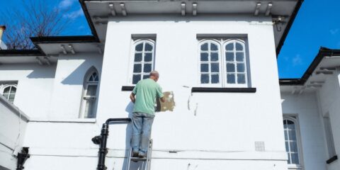 man in yellow shirt and blue denim jeans standing on white concrete building during daytime