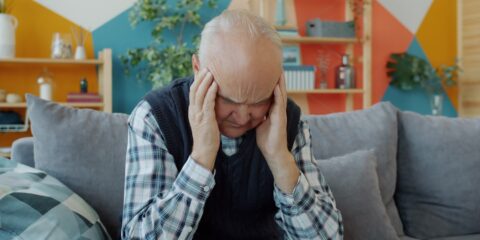 Elderly man holding head in discomfort on couch