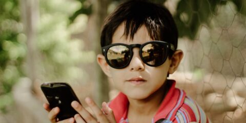 woman in red white and blue plaid scarf wearing black sunglasses holding black smartphone