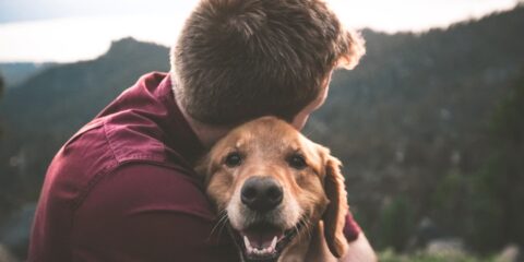 photo of man hugging tan dog